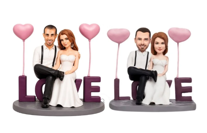 Romantic wedding cake toppers: a couple in formal attire sitting with pink heart balloons and the word LOVE on a base.