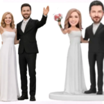 Two wedding cake toppers: a couple on the left with a bride in a white gown and groom in a black suit raising their arms in celebration; another couple on a pedestal—the bride in white and the groom in black suit—also waving.
