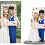 Smiling bride and groom hold a white frame decorated with colorful hearts outdoors.