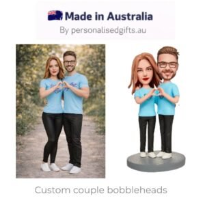 Real couple in matching blue shirts making a heart with their hands beside custom bobblehead figurines.