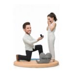 Man kneeling and proposing to a surprised woman, opening a ring box on a round platform with a 'Marry me' heart prop.