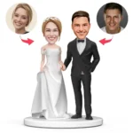 Cartoon wedding cake topper showing a bride in a white gown and groom in a black tuxedo on a round base, with two circular insets of real faces connected by arrows.