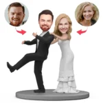 Wedding cake topper featuring a bride and groom figurine on a gray base, with circular photo heads of two people attached to each head.