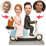 Caricature wedding cake topper: bride and groom ride a blue scooter with a gift basket on the back; circular portrait placeholders above indicate customizable faces.