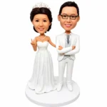 Wedding cake topper with a bride in a white gown and a groom in a white suit on a circular base, set against a white background