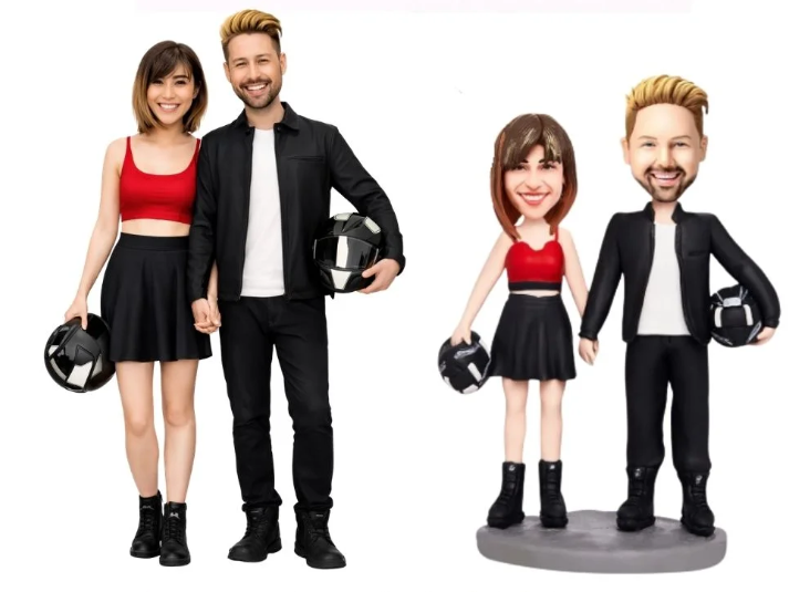 Real couple standing with two matching bobblehead figurines; all wear red tops and black outfits and hold black helmets.