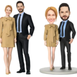 Two adults in business attire posing beside a cartoon-style miniature couple on a round base, matching outfits.