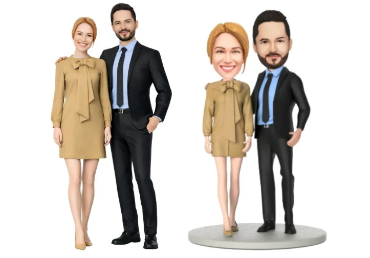 Two adults in business attire posing beside a cartoon-style miniature couple on a round base, matching outfits.