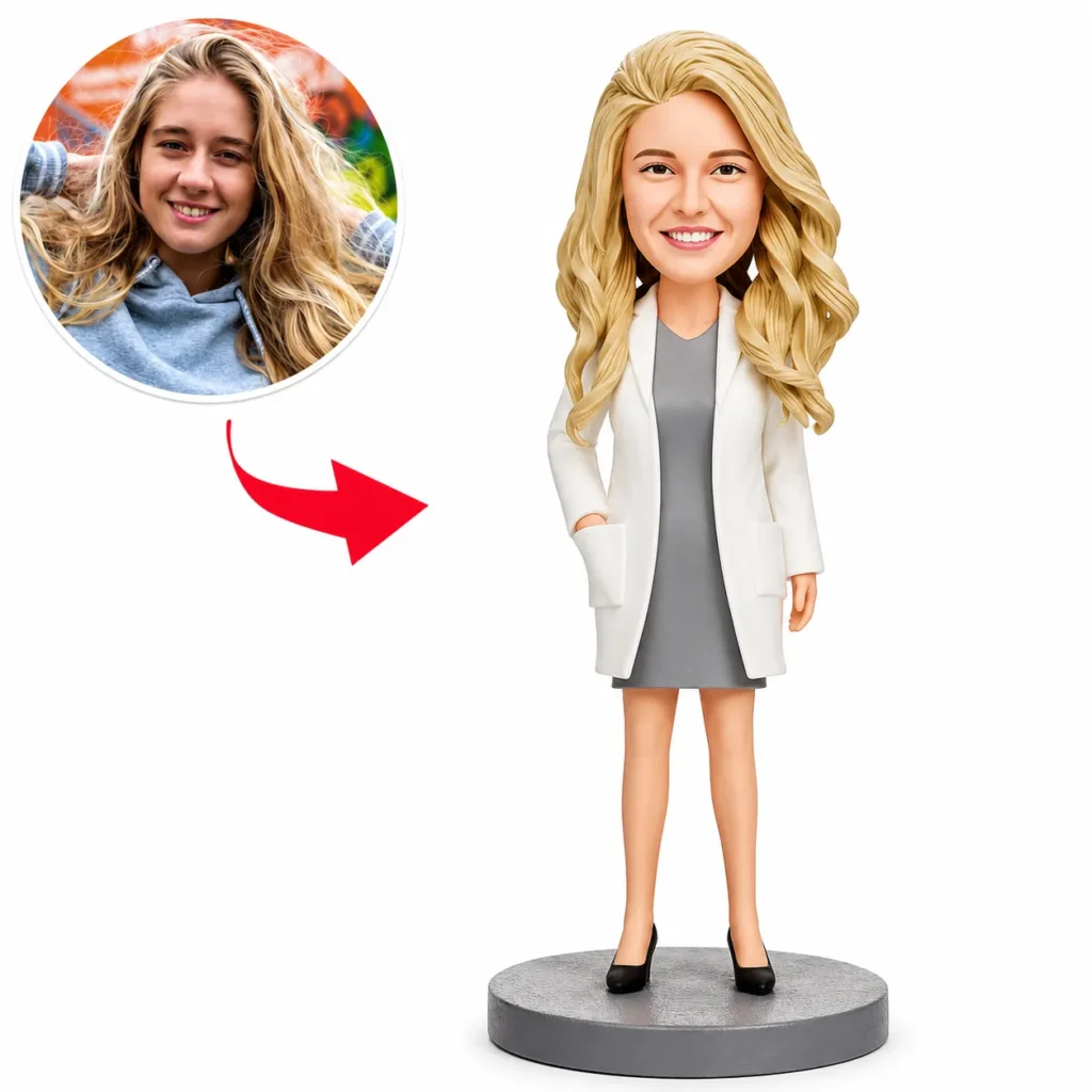 Bobblehead figure of a smiling blonde woman in a gray dress and white blazer on a round gray base; inset photo shows the same woman in a hoodie, with a red arrow linking the photo to the figure.