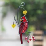 Stained-glass cardinal ornament hanging from a curved metal branch with yellow leaves and red berries.