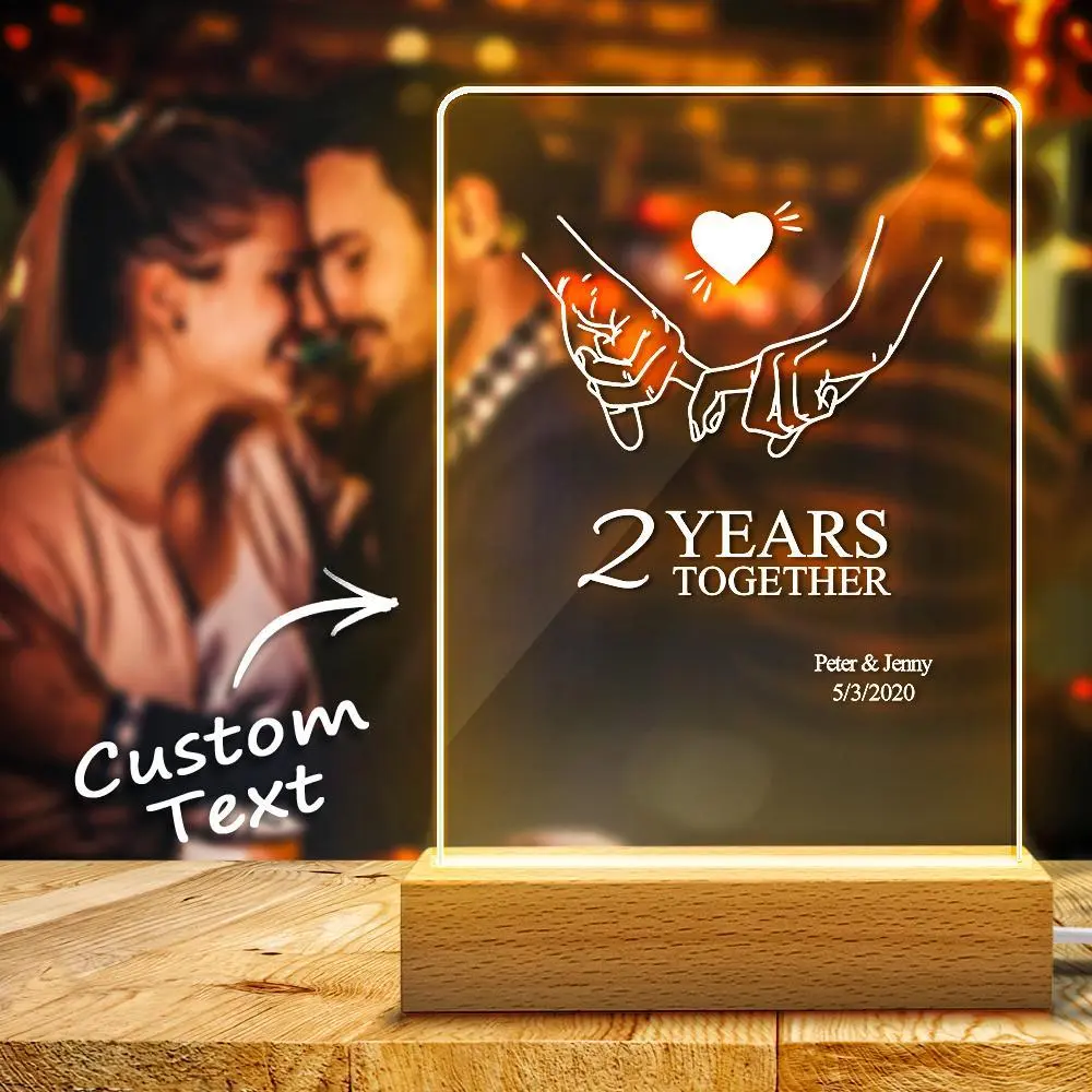 Illuminated acrylic sign on a wooden base reading '2 YEARS TOGETHER' with clasped hands and heart, plus names and date below (custom text)
