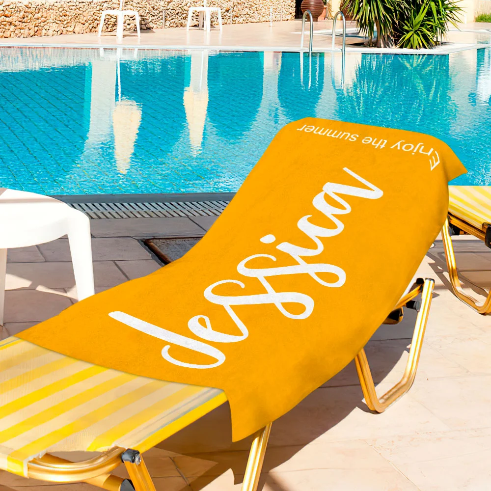 Orange poolside towel with 'enjoy summer' script draped over a striped yellow lounge chair beside a blue swimming pool.