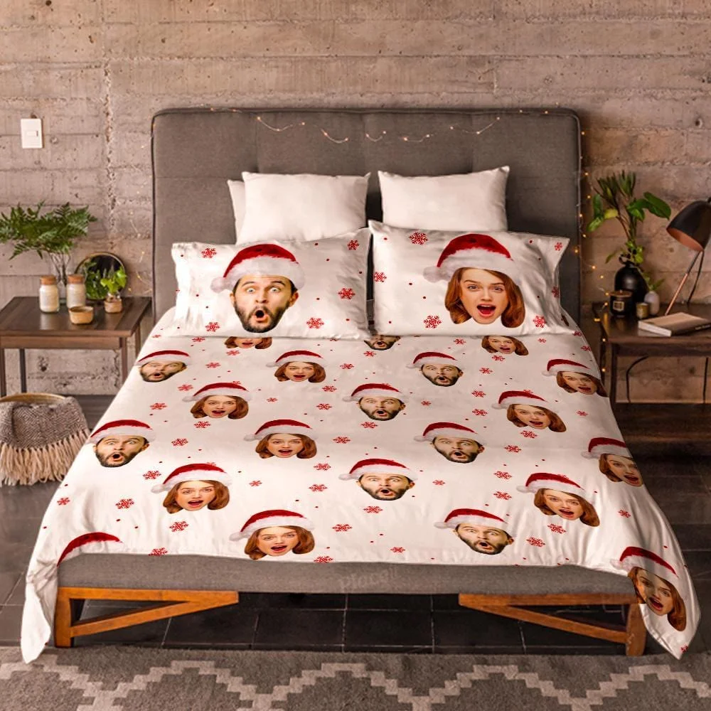 Bed with white Christmas duvet featuring repeated faces wearing Santa hats and red snowflakes on a grey upholstered headboard bed.