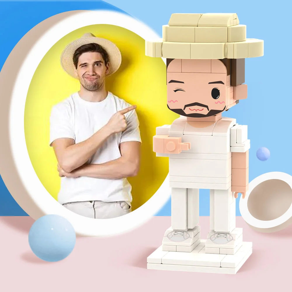 Man in a white shirt and straw hat points at a large LEGO-like statue of a man in white against a pastel pink and blue backdrop.