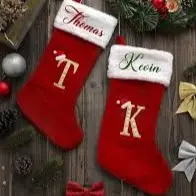 Two red Christmas stockings with white cuffs hanging on a wooden surface; left stocking reads 'Thomas' with a large 'T', right stocking reads 'Keon' with a large 'K'.
