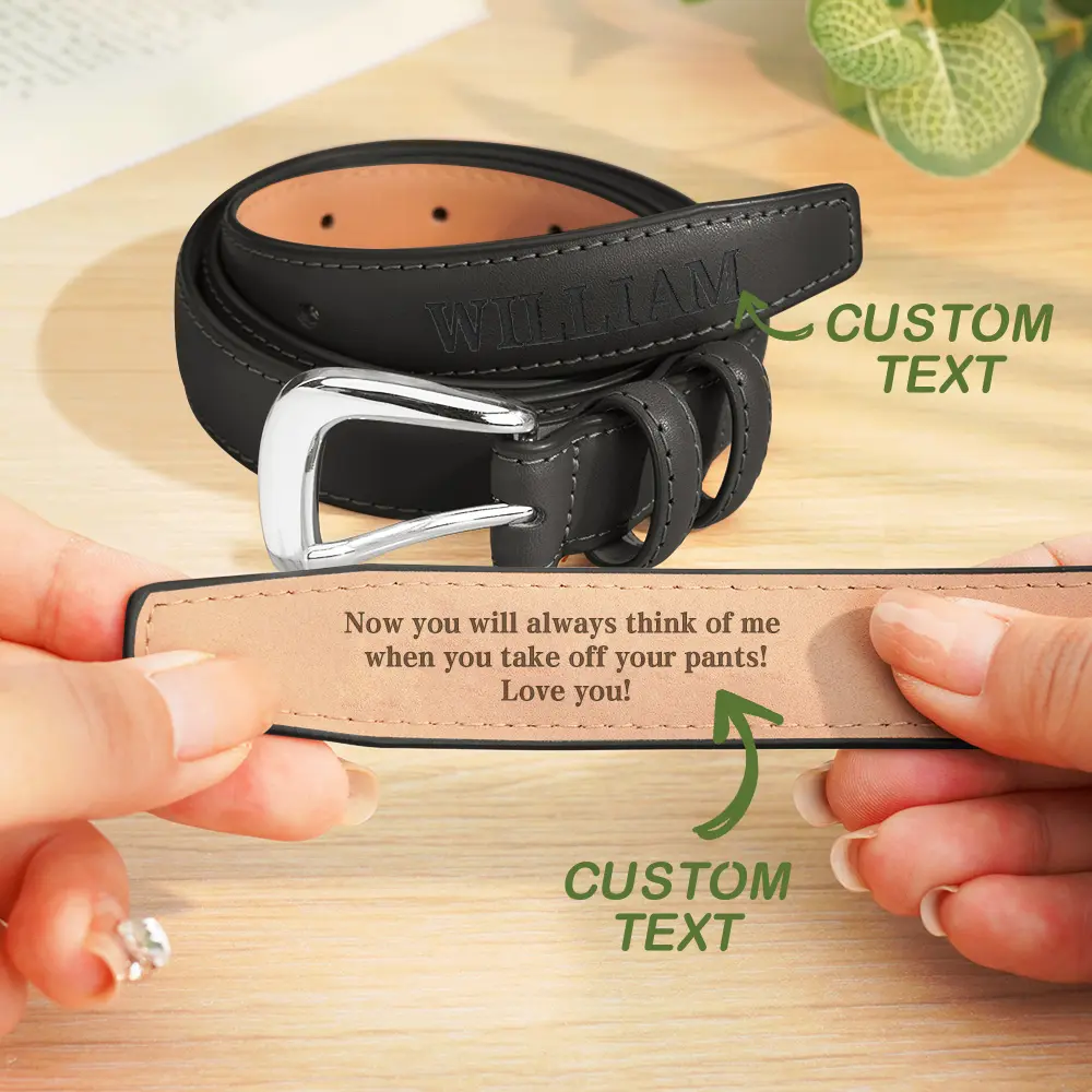 Black leather belt with a silver buckle, being held to show a tan strap area for custom text and a sample message on the inner strap.