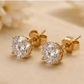 Pair of gold stud earrings with large round-cut clear stones on a pale beige surface.
