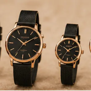 Pair of gold-tone wristwatches with black dials and black fabric straps, a larger men's watch on the left and a smaller women's watch on the right, displayed on a beige surface.
