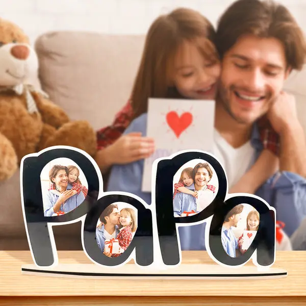 Wooden 'Papa' photo sign filled with family pictures on a table, with a father and daughter hugging in the background.