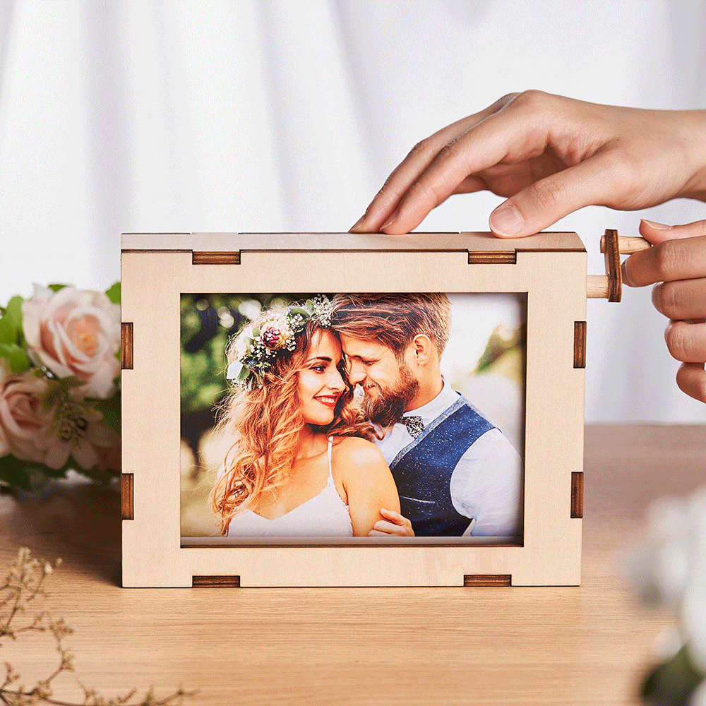 A wooden hinged picture frame on a table displaying a smiling couple's wedding photo, with hands opening the frame edge.