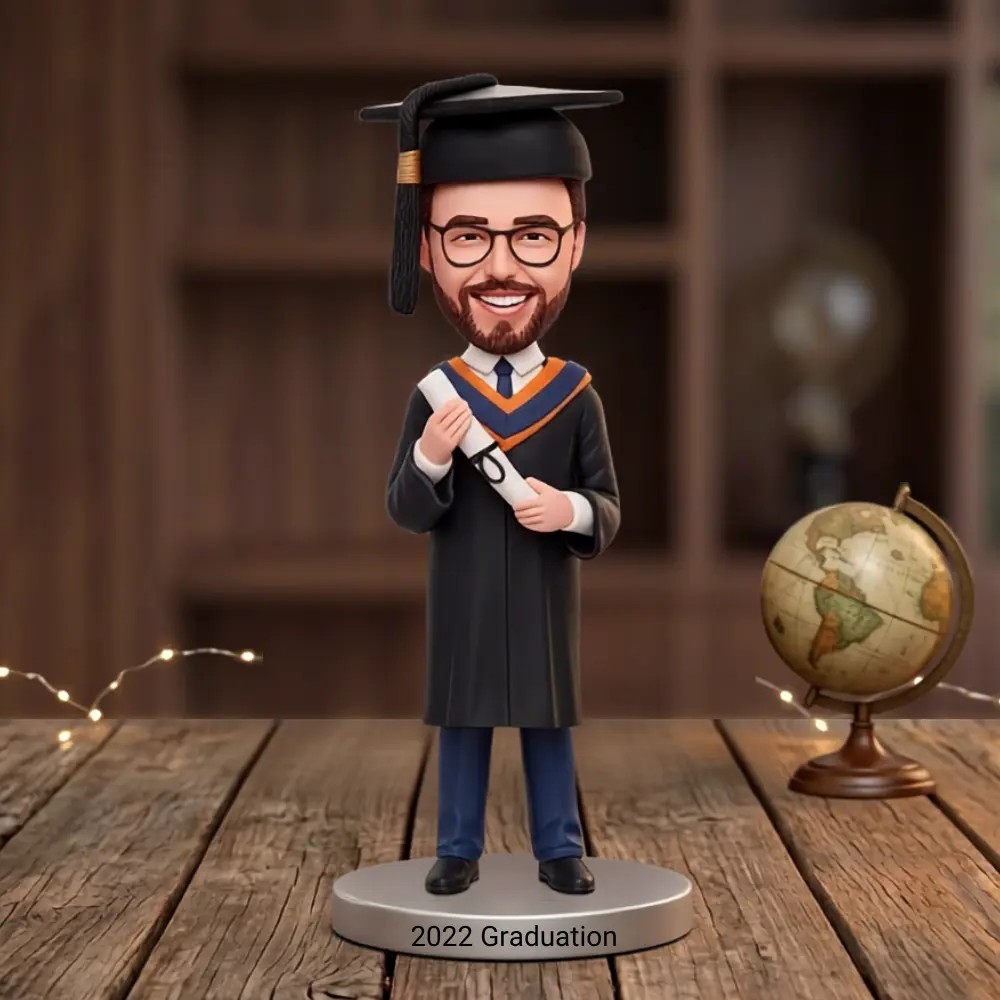 Graduation bobblehead figure in cap and gown holding a diploma, standing on a base reading 2022 Graduation with a globe nearby.