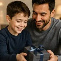 Father and son smiling while holding a wrapped gift with a blue ribbon together at home.",