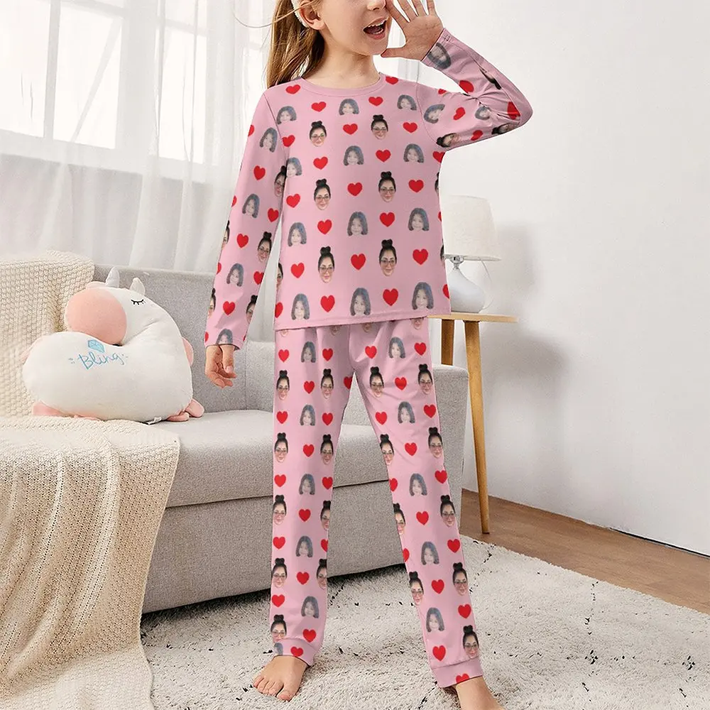 Young girl wearing pink pajamas with red hearts and small face portraits, standing in a living room.