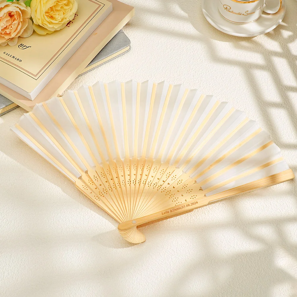 Open wooden hand fan with white fabric and pale gold stripes, spread on a light surface beside books and a teacup.