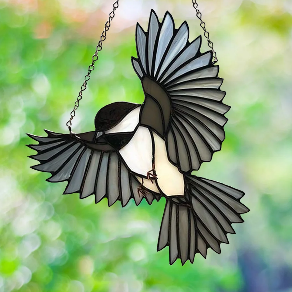 Stained-glass magpie suncatcher hanging by chains with wings spread in flight against a green background