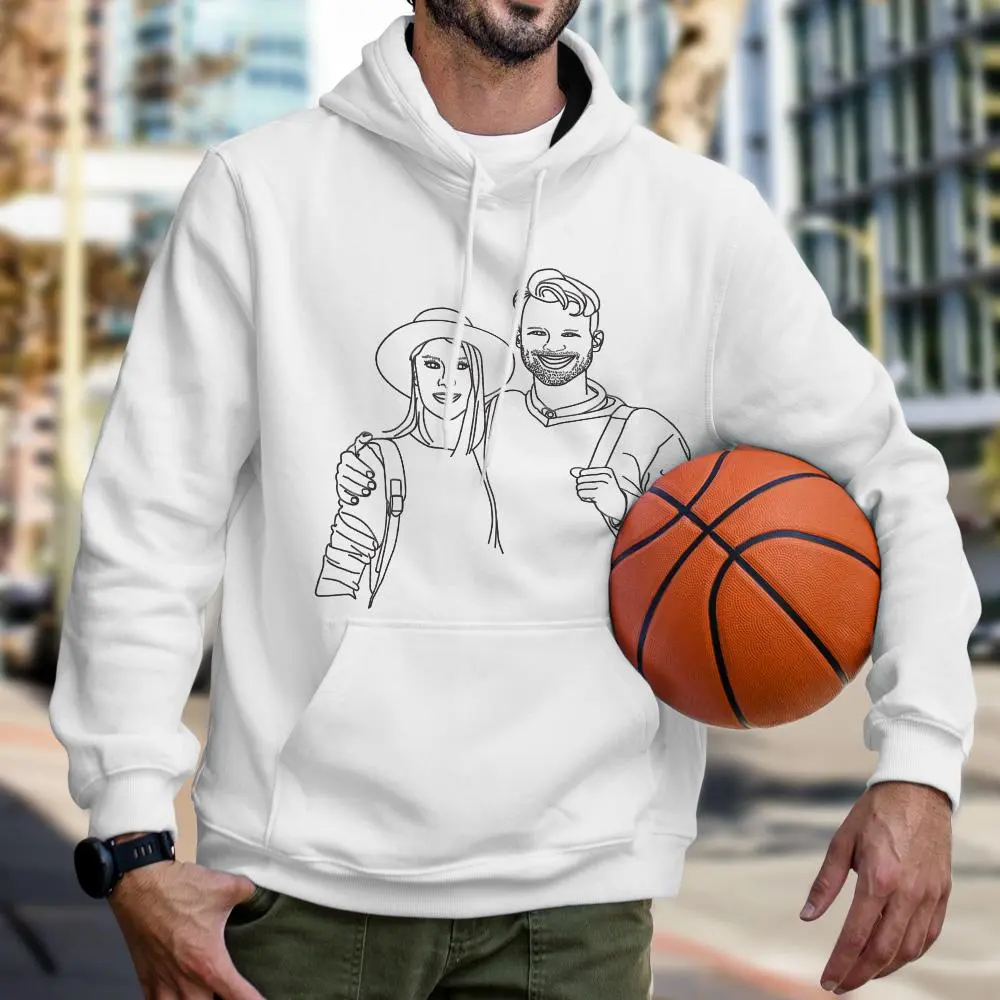 Person wearing a white hoodie with a line-drawn illustration of a couple on the chest, while holding a basketball under one arm, in an urban outdoor setting