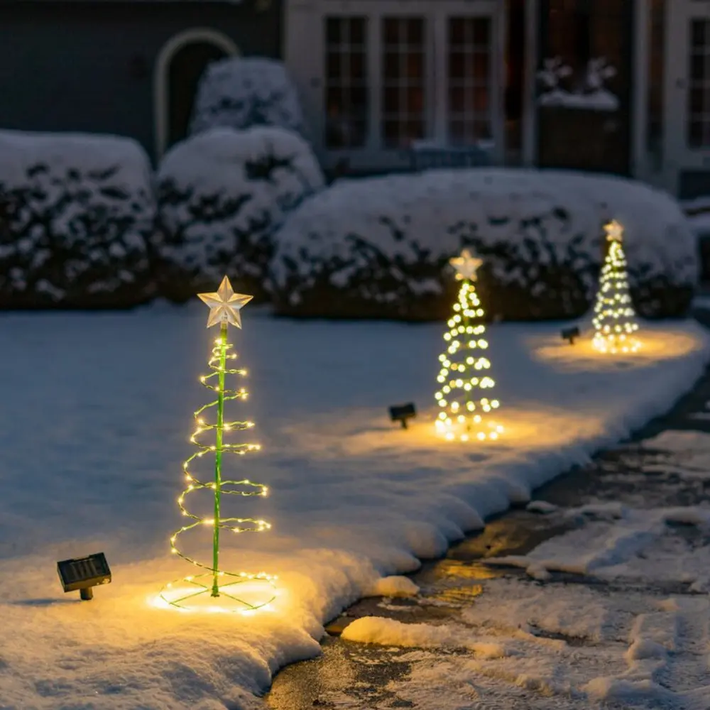 Snow-covered front yard with small illuminated Christmas tree decorations along a walkway, each tree topped with a star and glowing warm lights at dusk.