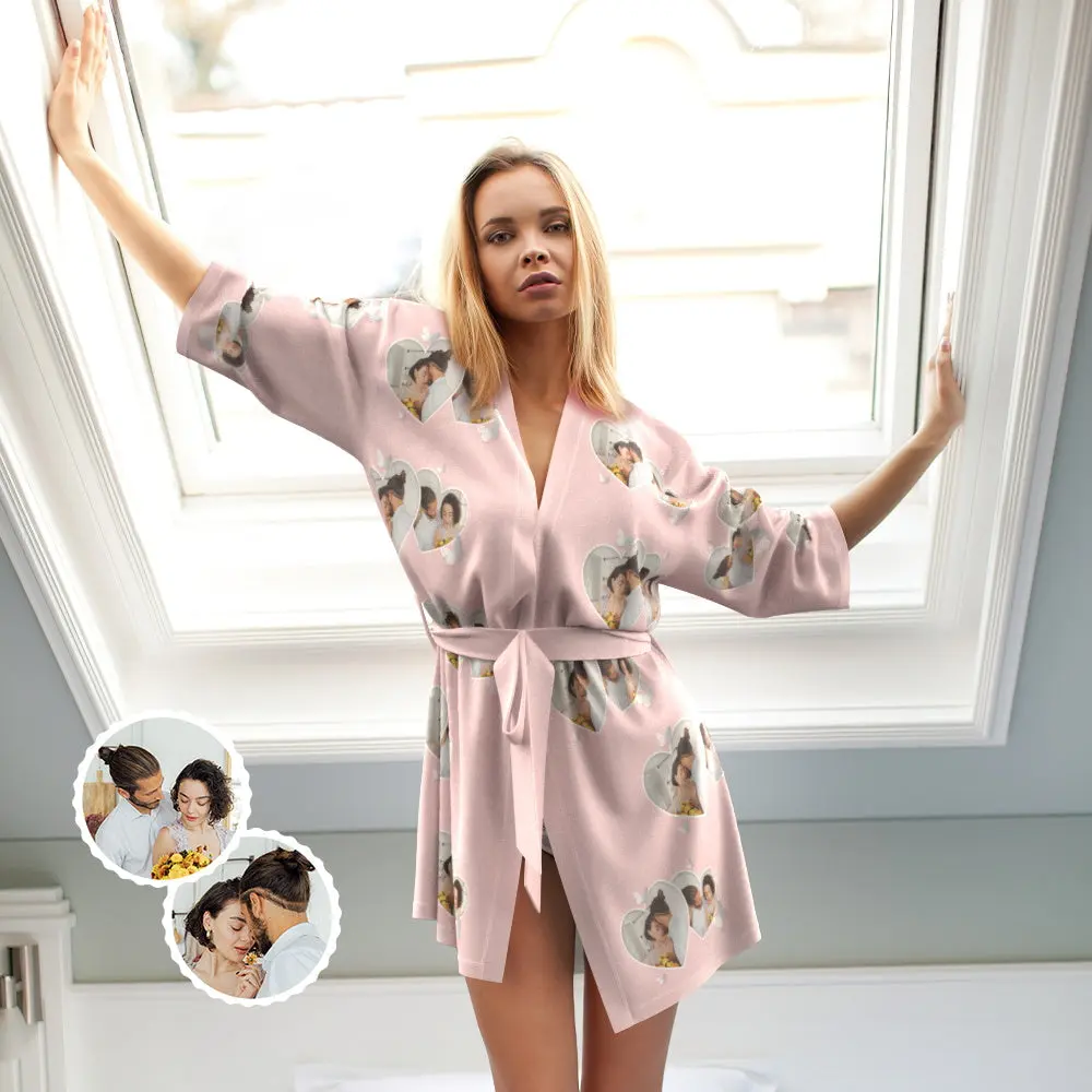 Woman in a pink robe with heart-shaped photo prints standing by a window, arms raised.