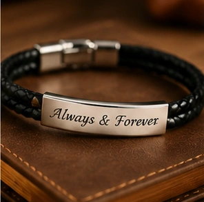 Black braided leather bracelet with a curved metal plate engraved 'Always & Forever'.