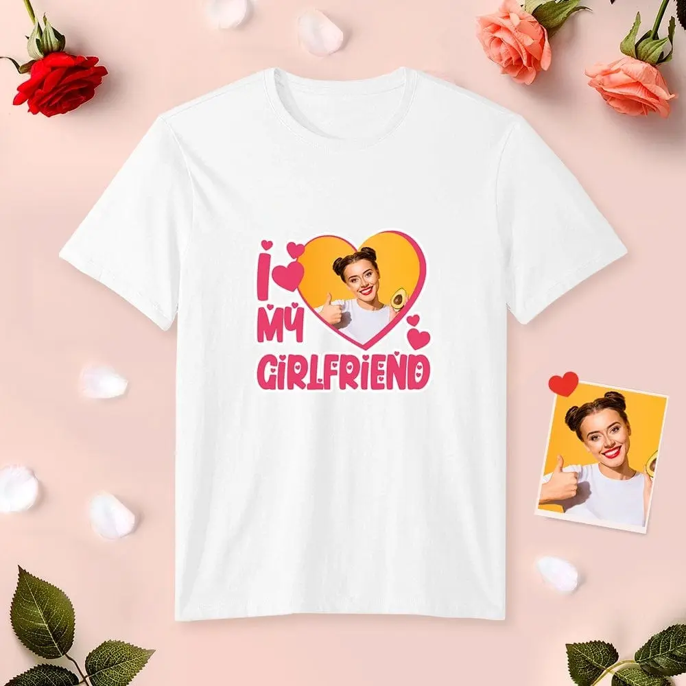 White T-shirt with a pink heart graphic and the text 'I ❤️ MY GIRLFRIEND'; inside the heart is a photo of a smiling woman giving a thumbs up. Rose-themed background.
