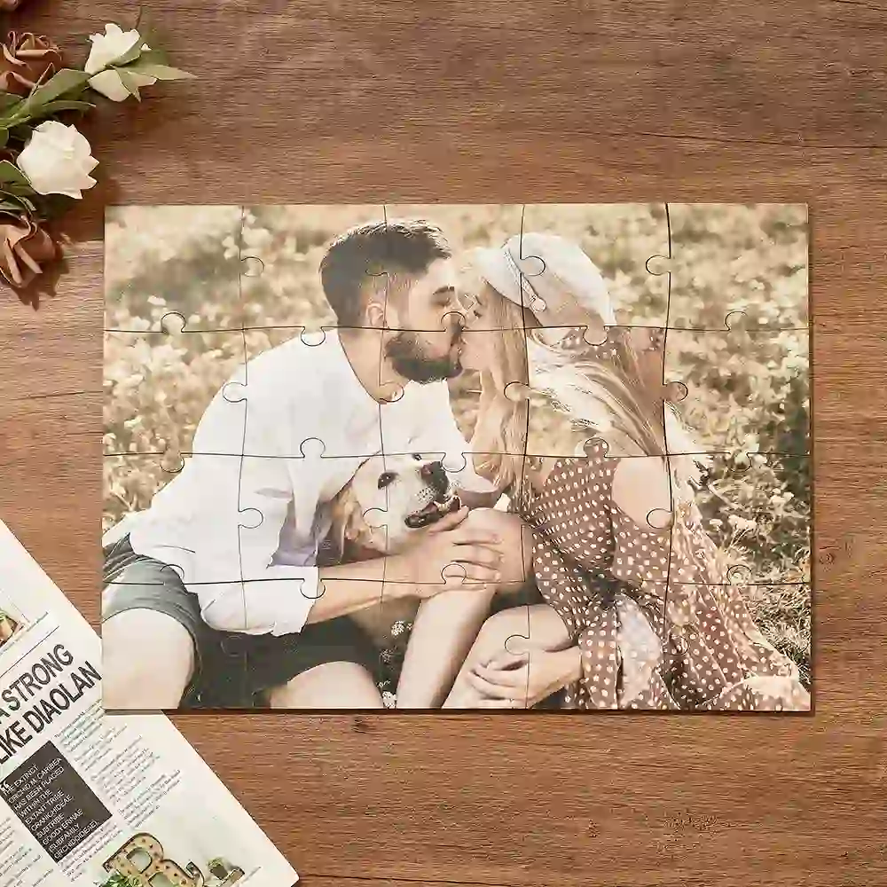 A completed jigsaw puzzle showing a couple kissing with a small dog between them on a wooden table.