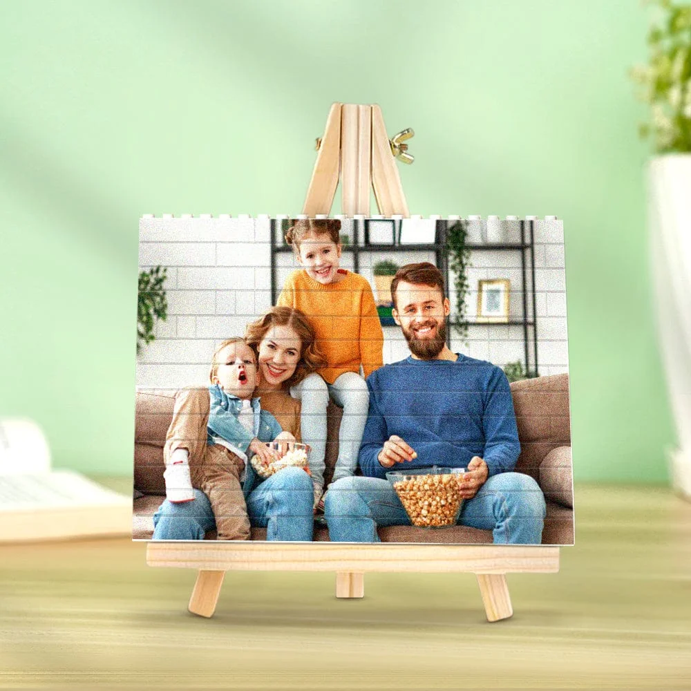 Family of four smiles on a couch, sharing popcorn in a cozy living room photo on a small easel frame.