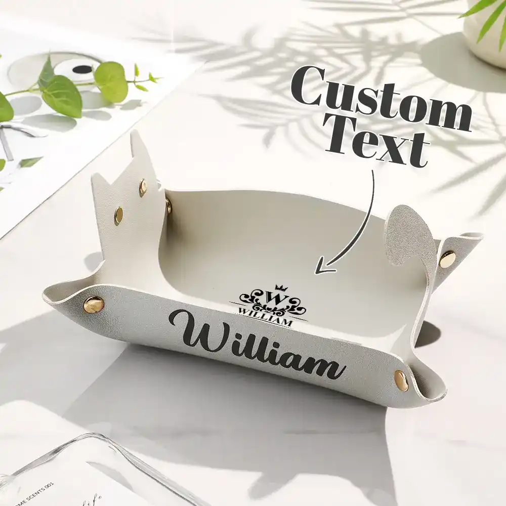 White personalized name tray showing the name 'William' with a crown emblem and 'Custom Text' placeholder on a clean desk surface, with green plant around.