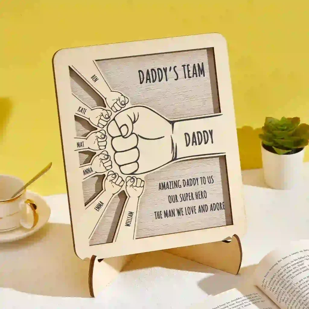 Framed cartoon poster titled 'Daddy's Team' showing a large fist with multiple smaller fists labeled with family member names surrounding it.