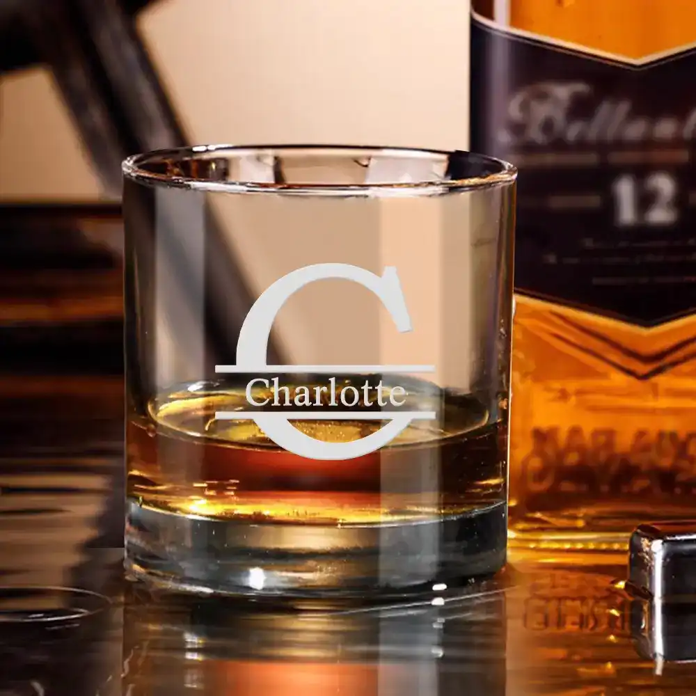 Whiskey glass with amber liquid and a white 'Charlotte' logo etched on it, with a bottle in the background.