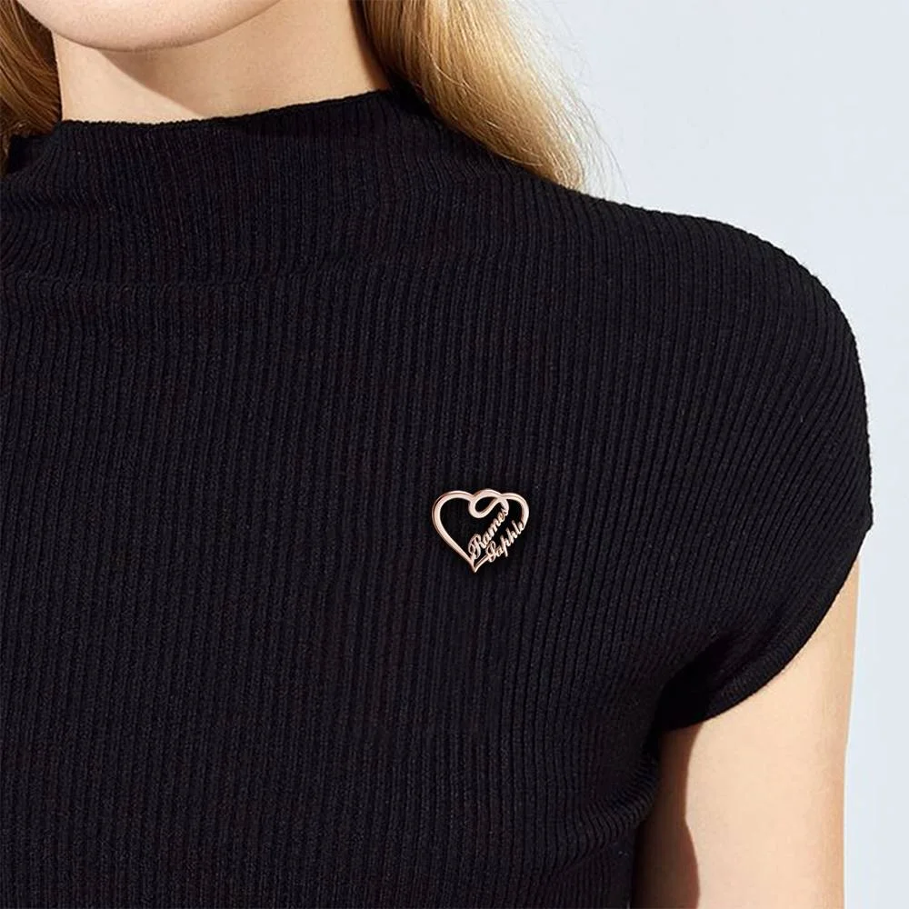 Close-up of a black ribbed top with a small gold heart-shaped pin on the chest, featuring cursive text.