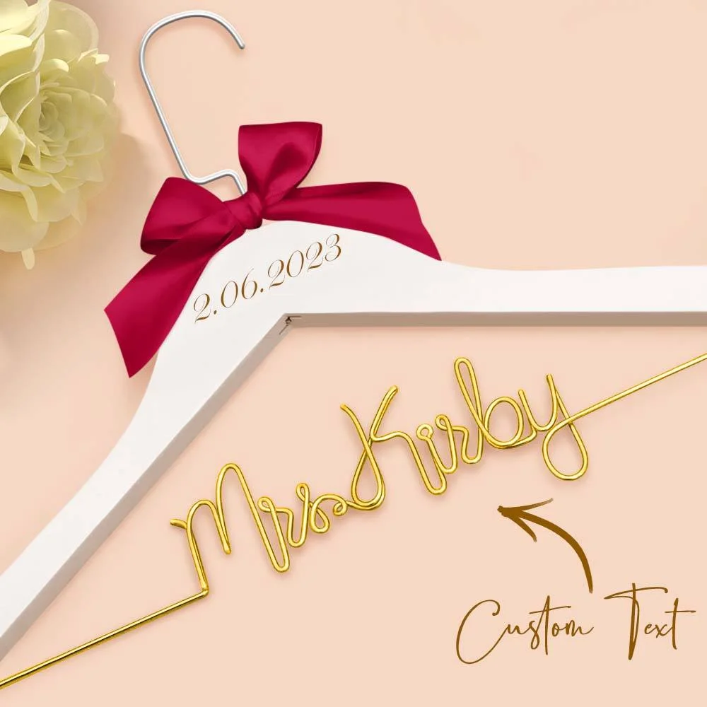 White dress hanger with a pink bow and a date tag reading 2.06.2023, set against a pale peach background; gold cursive text shows a customizable line (Custom Text).