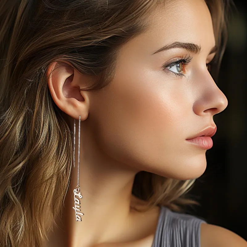 Close-up side profile of a woman wearing a long silver threader earring with a cursive pendant.