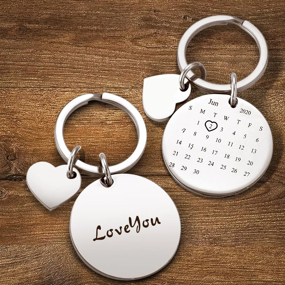 Silver keychain set with a circular calendar pendant and two heart charms on a wooden surface; engraving reads 'Love You'.