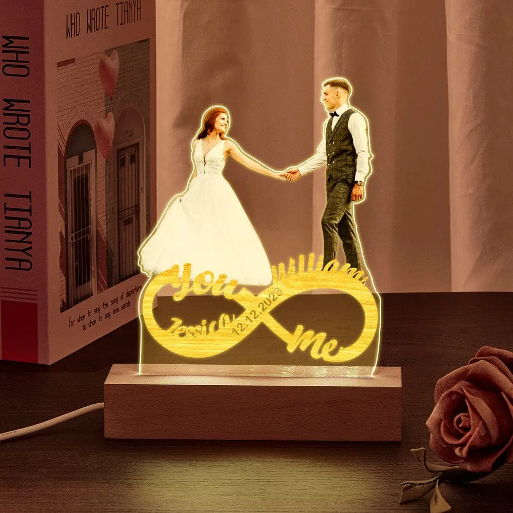 LED wedding keepsake with bride and groom figurines holding hands above an infinity-heart base, glowing warmly on a wooden stand.