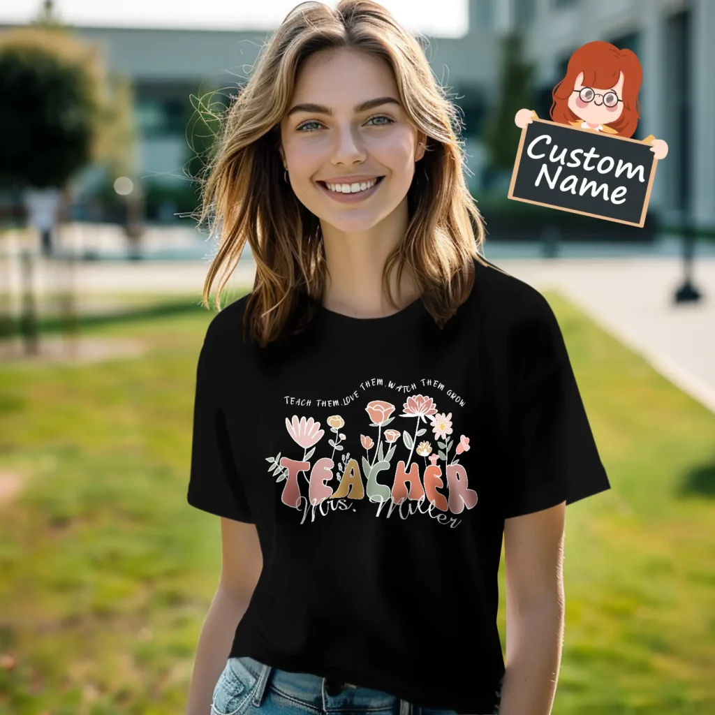 Smiling woman outdoors in a black floral shirt with a decorative, personalized “Teacher” graphic; cartoon sign reading “Custom Name” in the corner