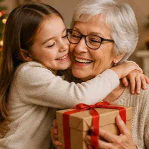 Young girl hugging a smiling grandmother who holds a wrapped gift during a tender moment.