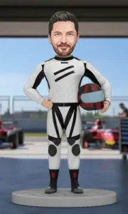 Bobblehead figurine of a race car driver in a white suit, holding a red-and-gray helmet, posed in a pit lane setting.