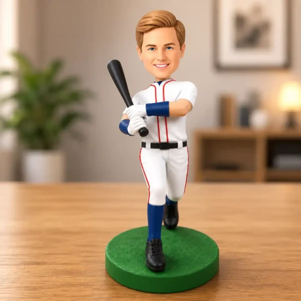 Bobblehead baseball player in white uniform with blue accents, holding a bat on a green base in a living room-like setting.
