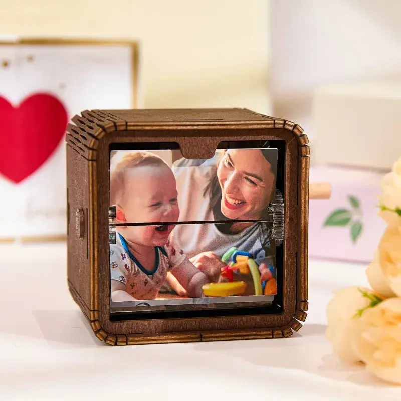 Wooden cube photo frame displaying a smiling woman with a baby playing with colorful toys in the reflection/photo inside the frame.