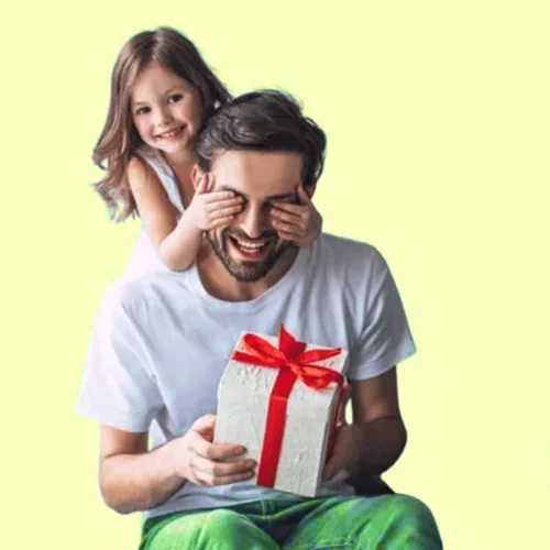 Little girl playfully covers dad's eyes while he smiles and holds a gift wrapped in white with a red ribbon, against a pale yellow background.